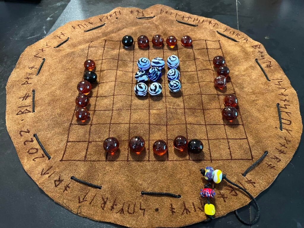 a picture of a leather hnefatafl gaming board with glass playing pieces on it